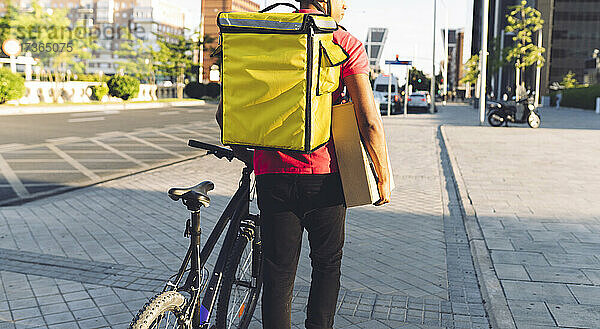 Zusteller  der ein Paket trägt  während er mit dem Fahrrad auf der Straße fährt