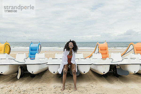 Fröhliche Frau lehnt sich am Strand an ein Boot