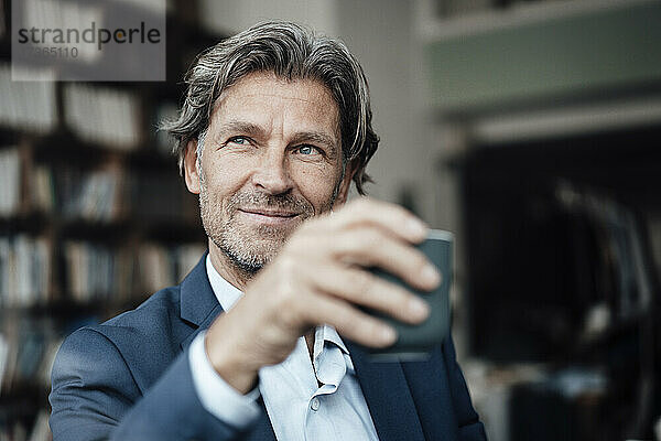 Lächelnder Geschäftsmann mit grauem Haar  der eine Kaffeetasse hält und in einem Café sitzt