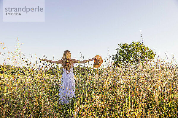 Junge Frau mit erhobenen Armen und Hut in einem Feld
