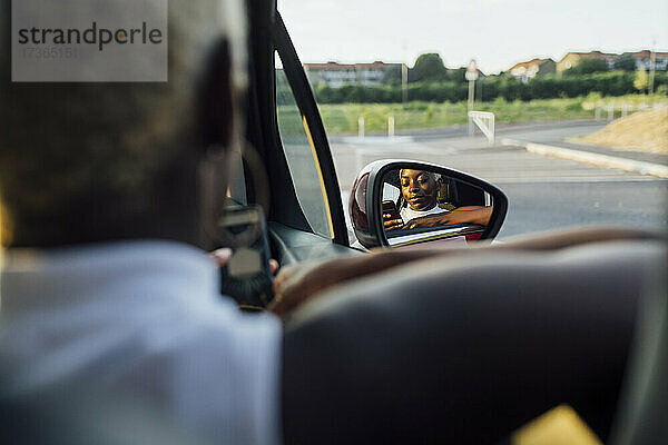 Reflexion einer Frau  die ein Telefon auf einem Autospiegel benutzt