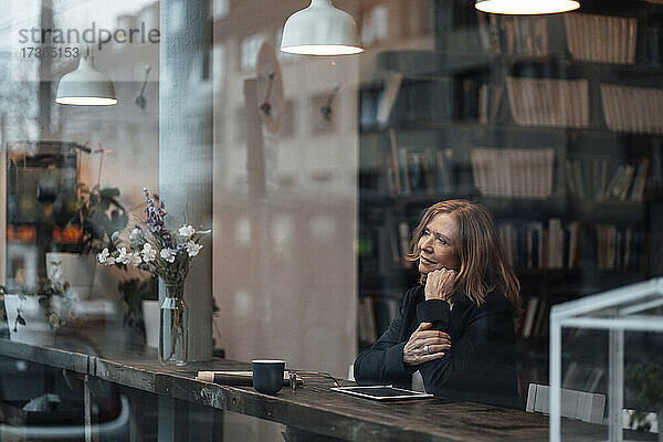 Nachdenkliche Geschäftsfrau sitzt im Café und schaut durch ein Glasfenster