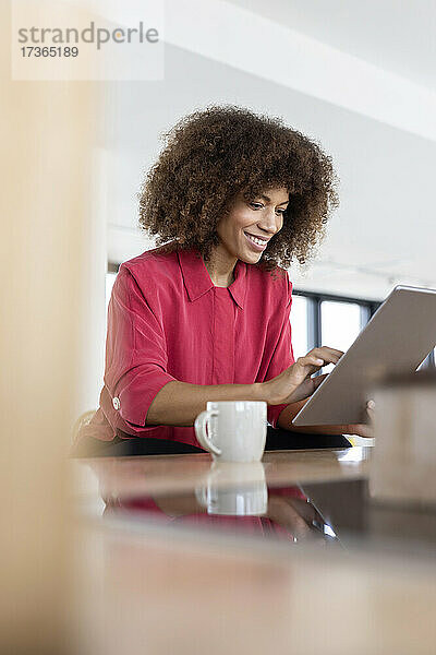 Weibliche Fachkraft lächelt  während sie ein digitales Tablet im Büro benutzt