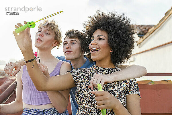 Junge multiethnische Freunde spielen mit Seifenblasen auf der Terrasse während einer Party