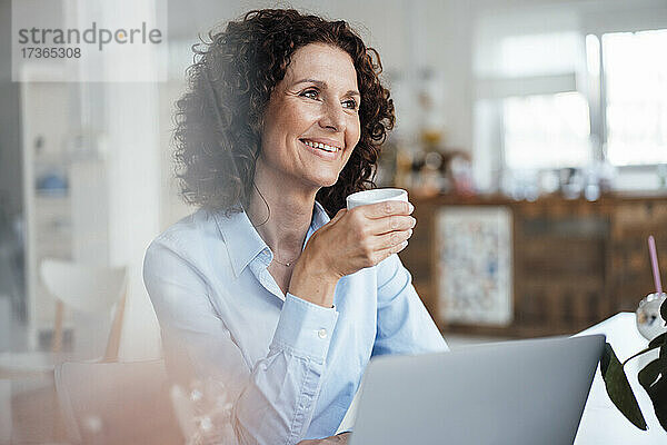 Lächelnde weibliche Fachkraft  die beim Kaffee trinken im Büro wegschaut