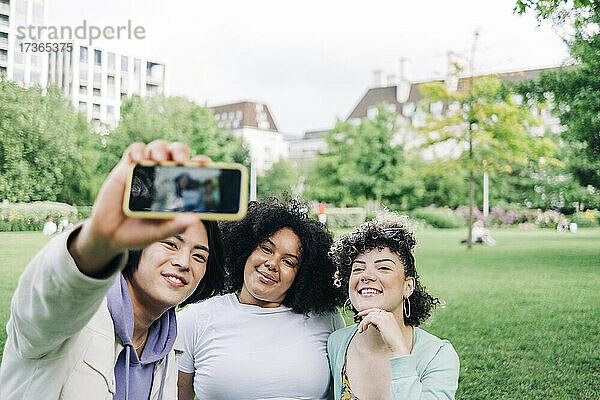 Lächelnde männliche und weibliche Freunde nehmen Selfie im Park