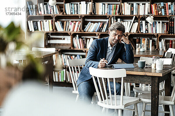 Reifer Geschäftsmann bei der Arbeit mit einem digitalen Tablet am Tisch im Café sitzend