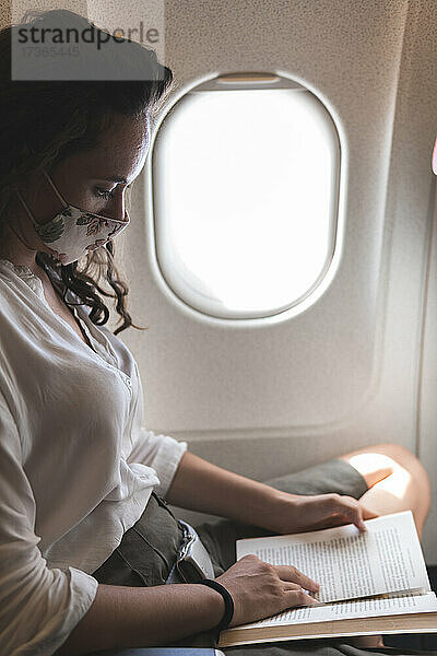 Geschäftsfrau liest ein Buch  während sie im Flugzeug während der COVID-19 reist