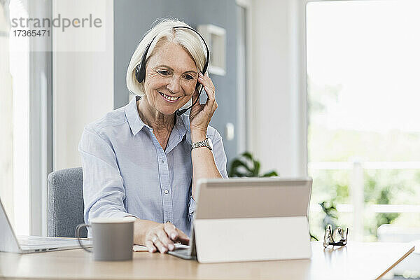 Verkäuferin stellt Headset ein  während sie im Büro zu Hause an einem digitalen Tablet arbeitet