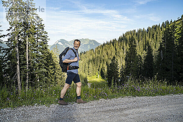 Männlicher Wanderer mit Rucksack  der über die Schulter schaut  während er auf einem unbefestigten Weg geht