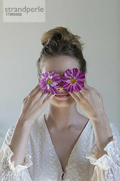 Junge Frau bedeckt Augen mit lila Blumen vor weißem Hintergrund