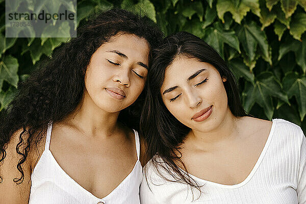 Multiethnische Schwestern mit geschlossenen Augen in der Nähe von Pflanzen