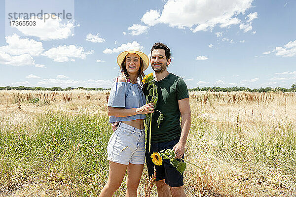 Lächelndes Paar hält Sonnenblumen auf einer Wiese