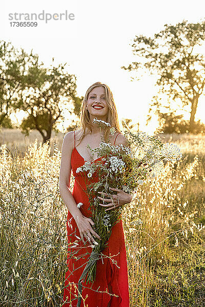 Lächelnde junge Frau hält Wildblumenstrauß im Feld