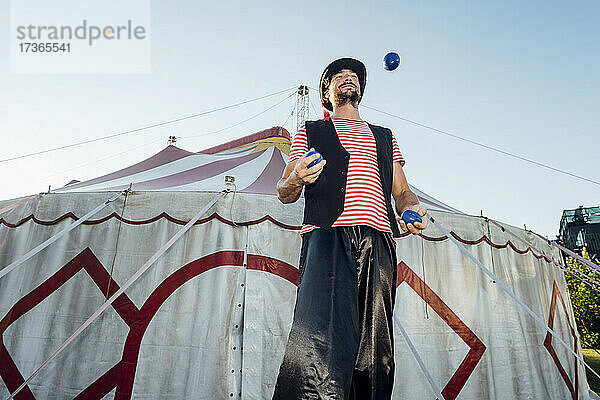 Männlicher Artist jongliert Bälle  während er vor einem Zirkuszelt steht