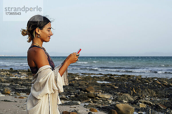 Lächelnde Frau mit Mobiltelefon am Strand