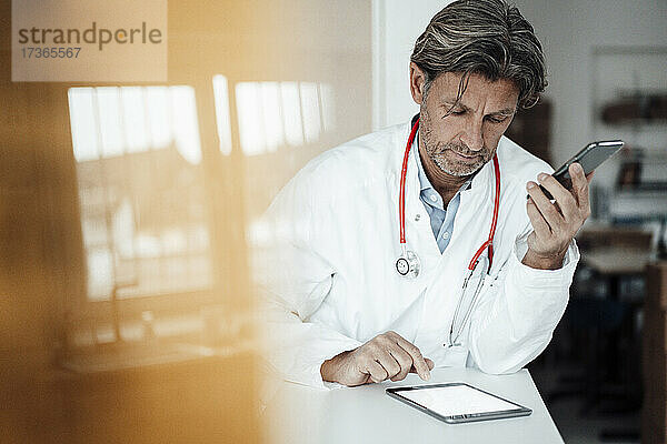 Männlicher Angestellter im Gesundheitswesen verwendet ein digitales Tablet  während er sich in einer Klinik auf den Schreibtisch stützt