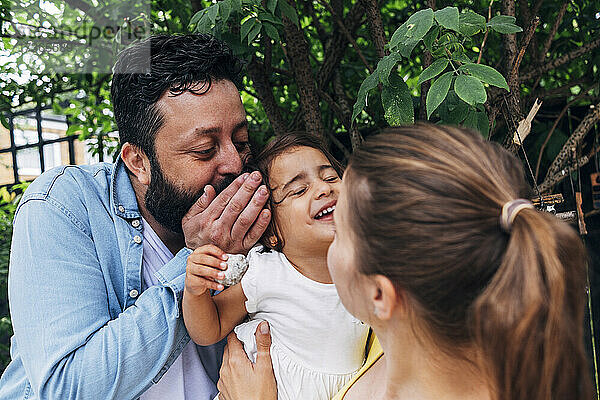 Vater flüstert seiner Tochter ins Ohr  während er mit seiner Mutter im Hinterhof spielt