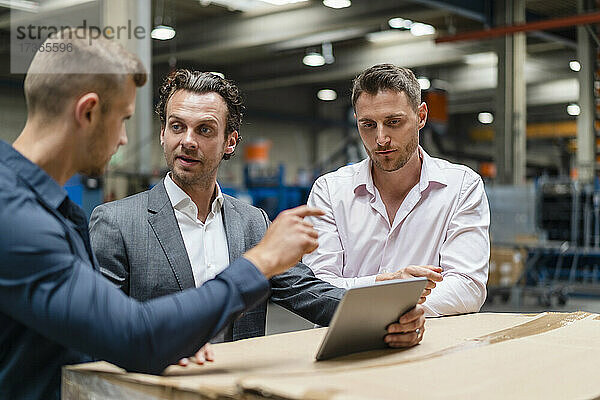 Männliche Kollegen diskutieren in einer Fabrik über ein digitales Tablet