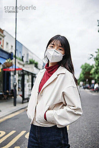 Junge Frau mit Händen in den Taschen und Gesichtsschutzmaske in der Stadt