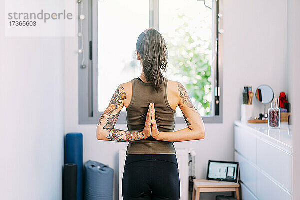 Frau mit hinter dem Rücken verschränkten Händen übt Yoga zu Hause