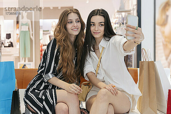 Frau nimmt Selfie mit lächelnden Freund durch Smartphone im Einkaufszentrum