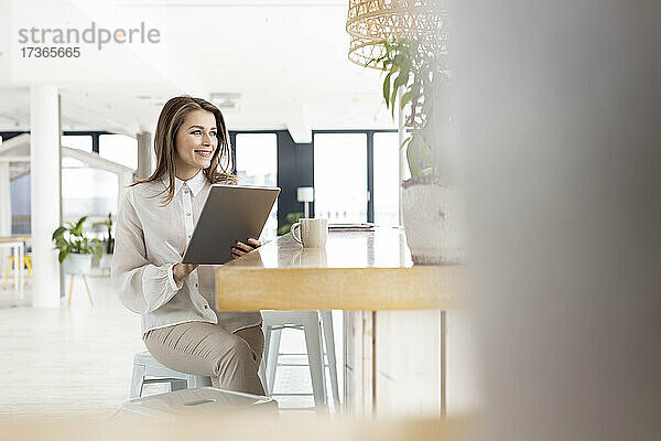 Weibliche Fachkraft mit digitalem Tablet auf einem Tisch im Büro sitzend