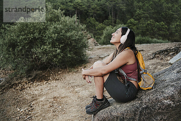 Weiblicher Rucksacktourist mit geschlossenen Augen  der auf einem Felsen sitzend Musik hört