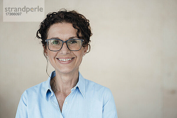 Lächelnde Geschäftsfrau mit Brille vor einer Wand stehend