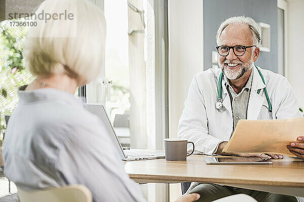 Lächelnder männlicher Arzt im Gespräch mit einer Patientin am Schreibtisch