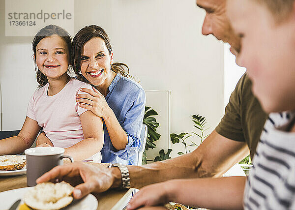 Lächelnde Tochter und Mutter betrachten den Vater beim Frühstück