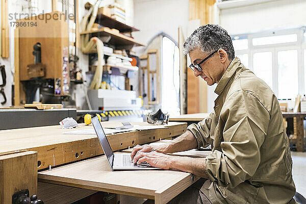 Älterer männlicher Tischler arbeitet in der Werkstatt am Laptop