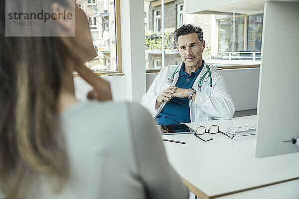 Männlicher Arzt im Gespräch mit einer Patientin im Büro