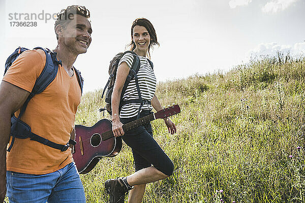 Lächelnde Frau mit Gitarre geht an einem Mann im Gras vorbei