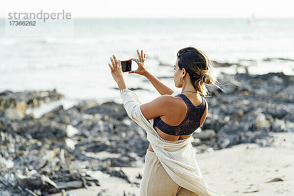 Frau hält Smartphone beim Fotografieren am Strand