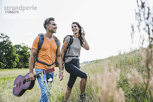 Lächelnde Frau schaut auf Mann mit Gitarre beim Wandern