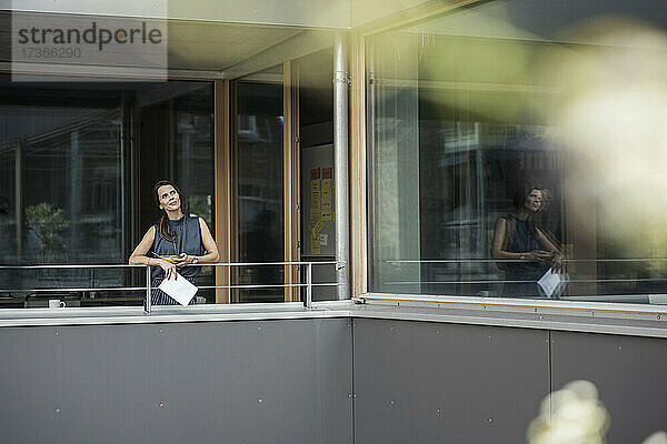 Geschäftsfrau mit digitalem Tablet  die auf dem Balkon eines Büros steht und nachdenkt