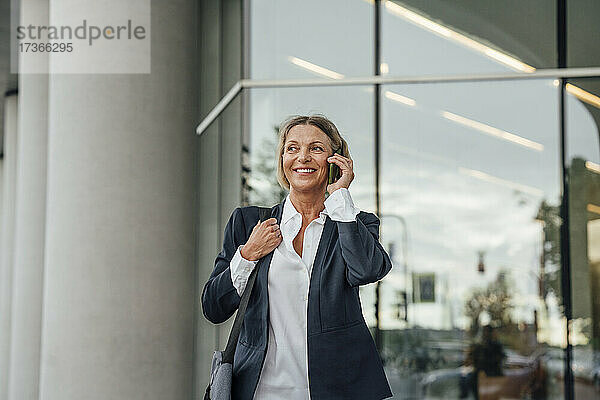 Lächelnde Geschäftsfrau  die im Büropark mit einem Mobiltelefon spricht