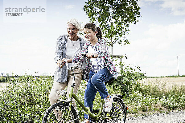 Lächelnde Frau unterrichtet ein Mädchen  das auf einem unbefestigten Weg Fahrrad fährt