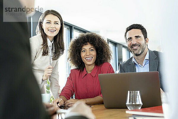 Lächelnde Kollegen mit Laptop bei einer Besprechung im Büro