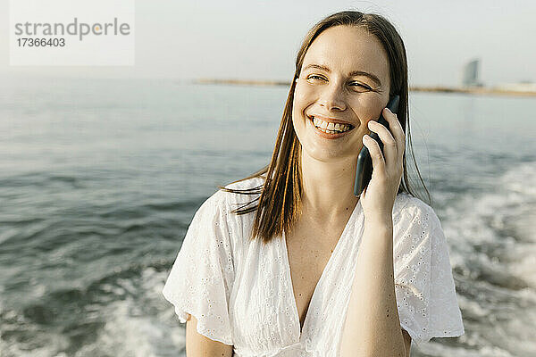 Glückliche Frau  die am Strand mit einem Mobiltelefon spricht
