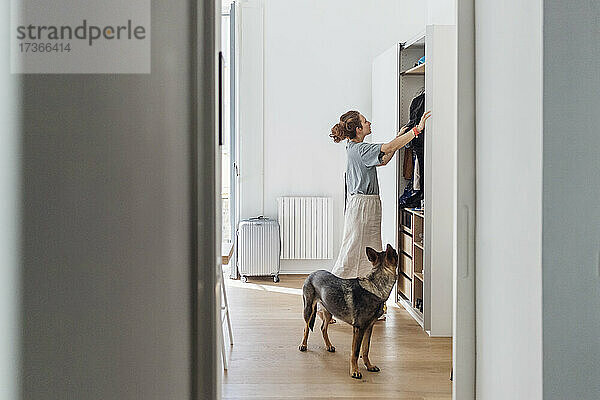 Frau schaut in den Kleiderschrank  während sie in der Wohnung neben dem Hund steht