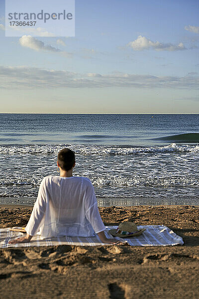 Frau schaut auf das Meer  während sie auf einer Decke sitzt