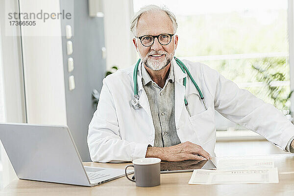 Lächelnder reifer männlicher Arzt am Schreibtisch