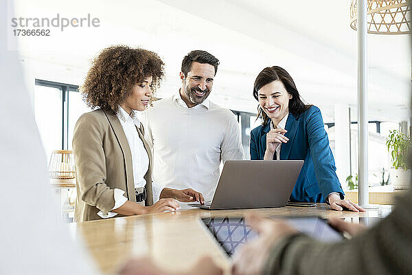 Glückliche männliche und weibliche Fachleute  die über einen Laptop im Büro diskutieren