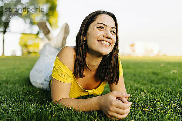 Glückliche junge Frau  die wegschaut  während sie sich im Gras entspannt