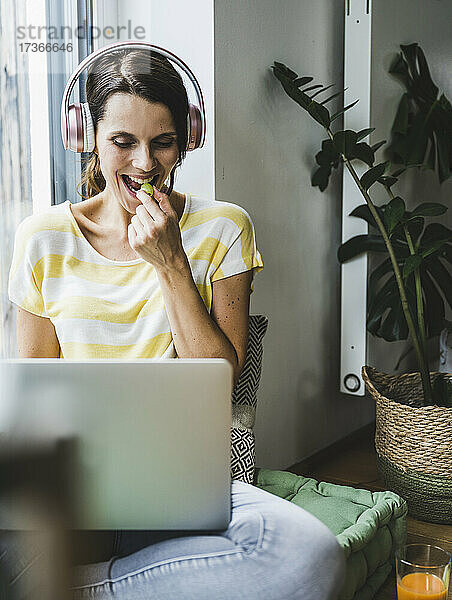 Frau isst eine Weintraube  während sie zu Hause einen Laptop benutzt
