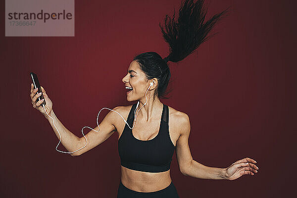 Weibliche Athletin  die springt  während sie Musik über ihr Smartphone hört