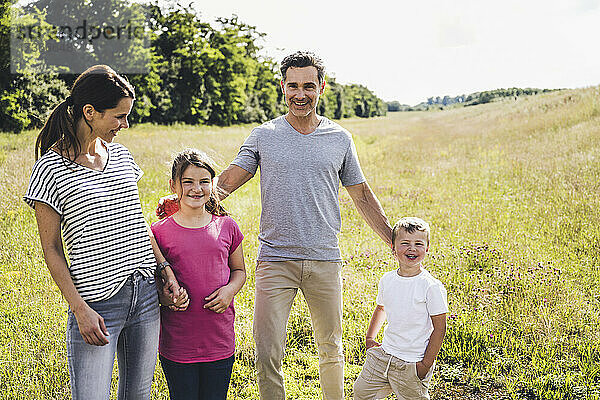 Lächelnde Eltern stehen mit Kindern auf einer Wiese an einem sonnigen Tag