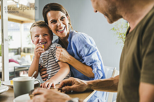 Lächelnde Mutter und Sohn betrachten den Vater beim Frühstück zu Hause